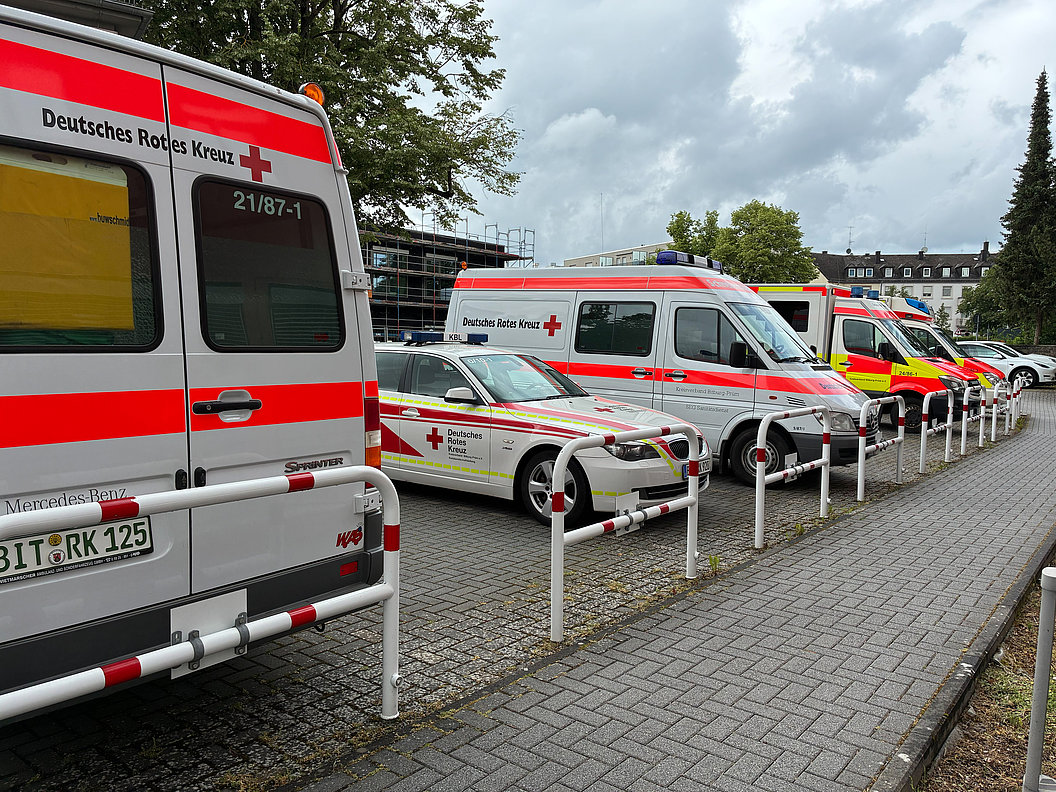 Mehrere Einsatzfahrzeuge des Deutschen Roten Kreuzes in einer Reihe auf einem Parkplatz bei bewölktem Himmel