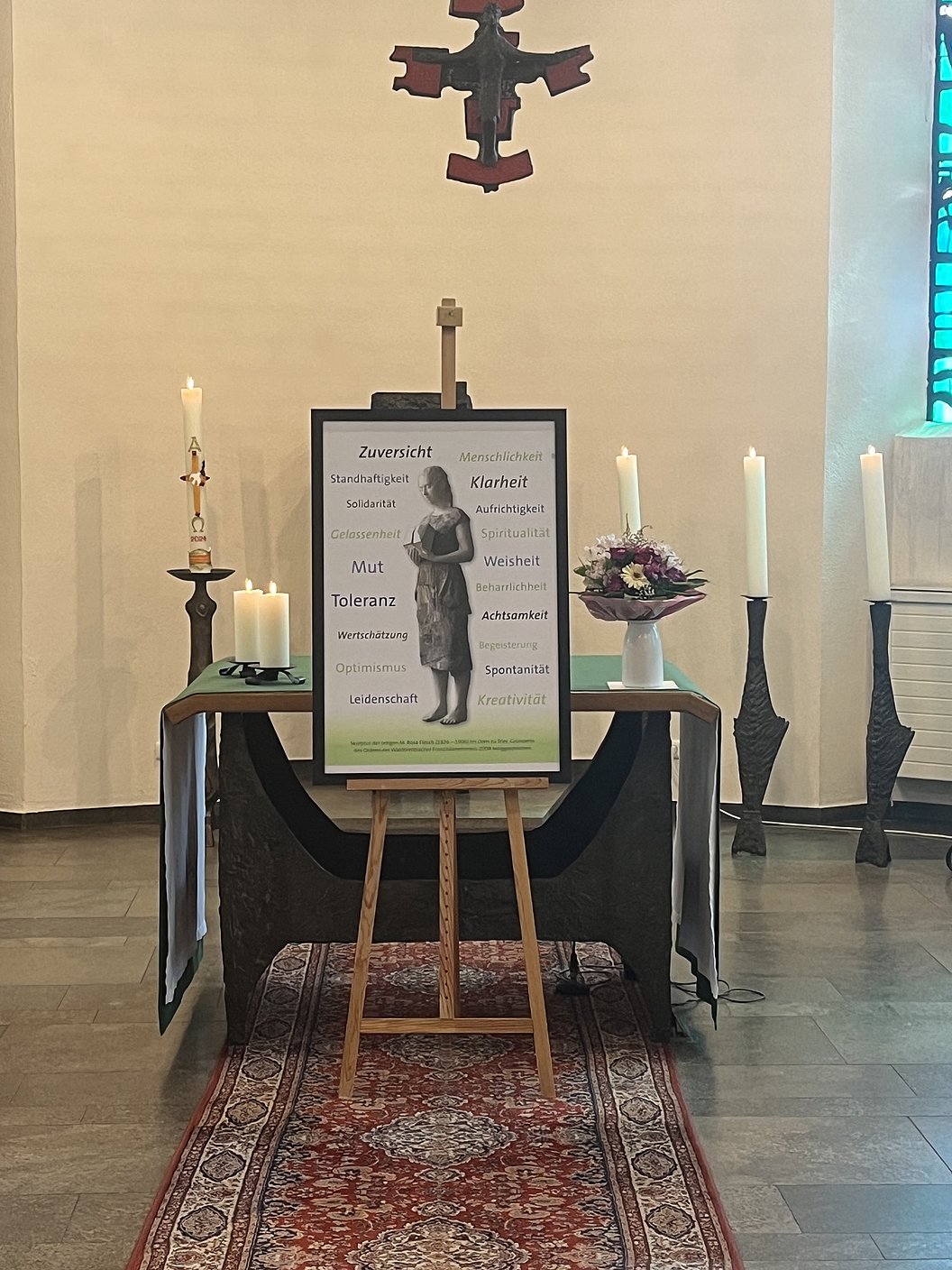 Altar mit Kerzen, Blumen und einem Bild auf einer Staffelei mit Worten wie 'Zuversicht', 'Mut' und 'Toleranz' in einer Kirche.