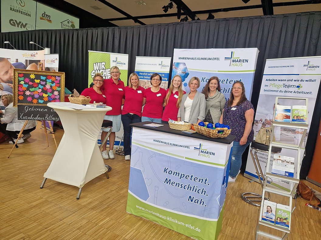 Mitarbeiter in roten Shirts und Besucher an Informationsständen des Marienhaus Klinikums Eifel auf einer Messe.